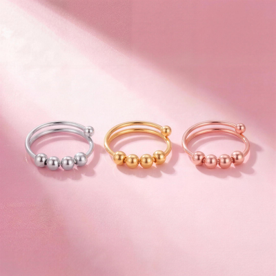 Fidget Beads Ring in Silber, Gold und Roségold liegend auf rosa Hintergrund