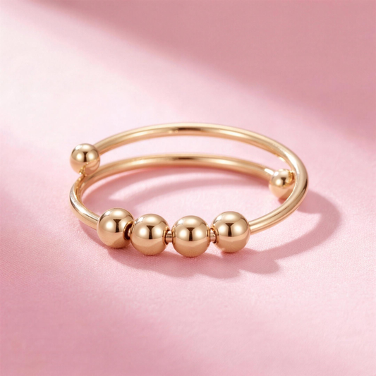 Fidget Beads Ring Gold mit vier drehbaren Perlen auf rosa Hintergrund