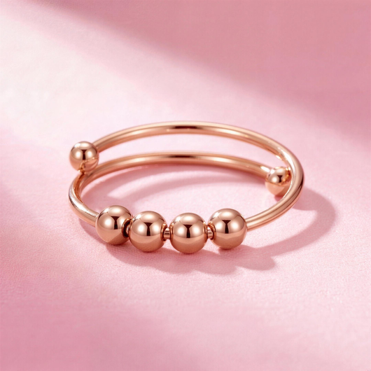 Fidget Beads Ring Roségold mit vier drehbaren Perlen auf rosa Hintergrund
