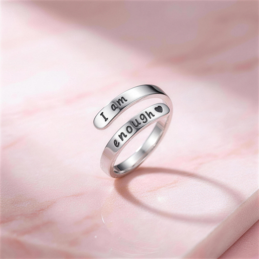 I Am Enough Ring – verstellbarer silberfarbener Wickelring mit Gravur „I am enough ♥“, stehend auf hellrosa Marmor