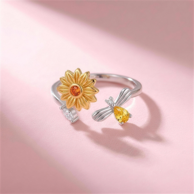 Bee Ring – silberfarbener verstellbarer Ring mit goldener Sonnenblume und Biene, liegend auf rosa Hintergrund